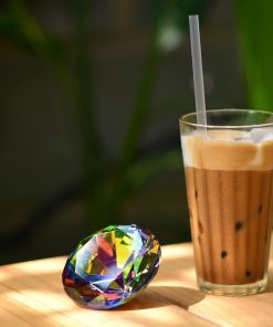 Glass of iced coffee and colorful gem on wooden table in sunlight, ideal for lifestyle and beverage themes.